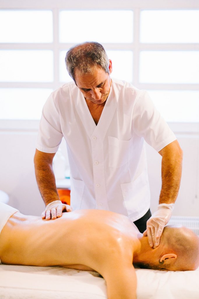 Masajista profesional aplicando masaje terapéutico en la espalda y cuello de un hombre tumbado